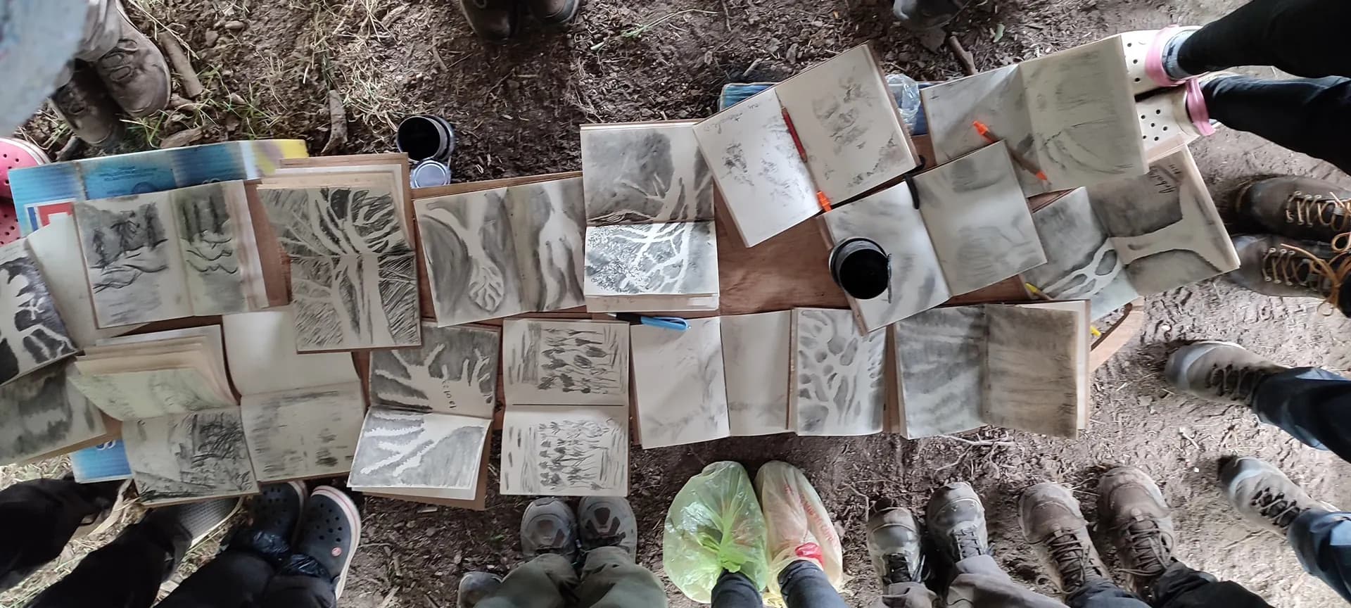 Cuadernos de dibujo abiertos en el suelo, en ronda entre los pies del grupo
