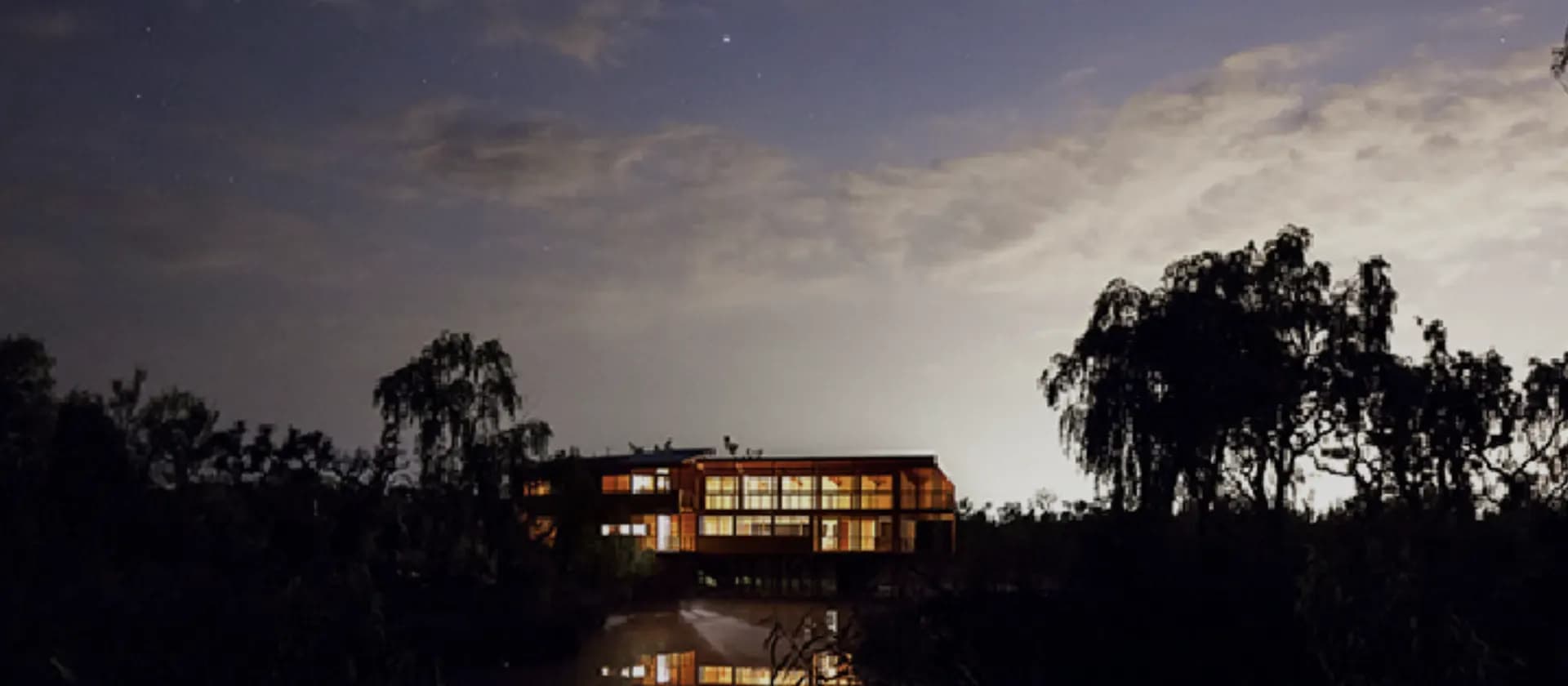 El Galpón del Pantano de noche, con las ventanas encendidas entre los árboles