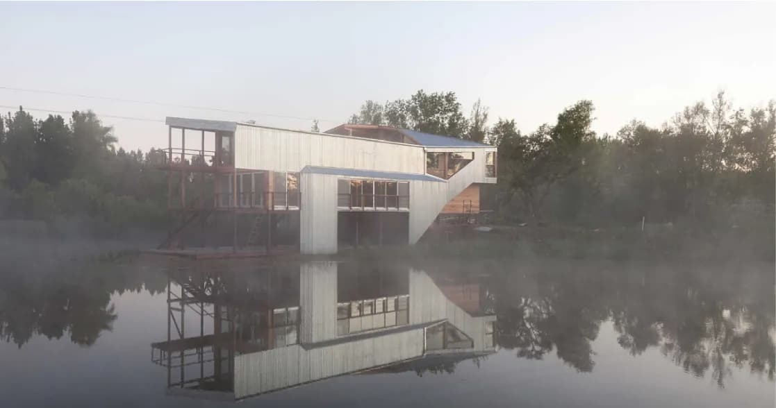 Una casa de madera sobre la laguna, reflejada en el agua entre la niebla